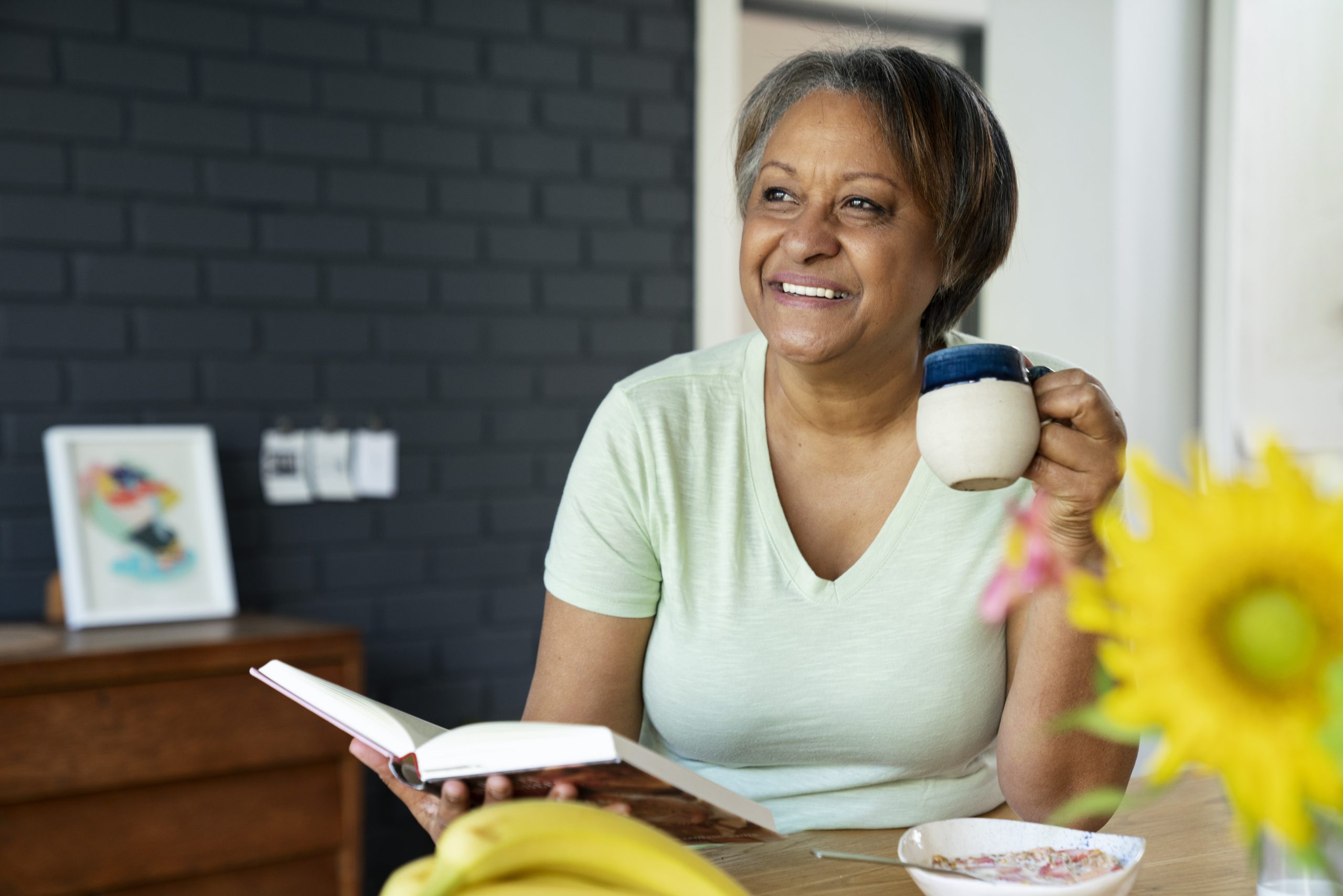 Woman holding an open book in one hand and a cup in the other illustrates blog "Is it a Good Idea to Switch to Medicare Advantage?"