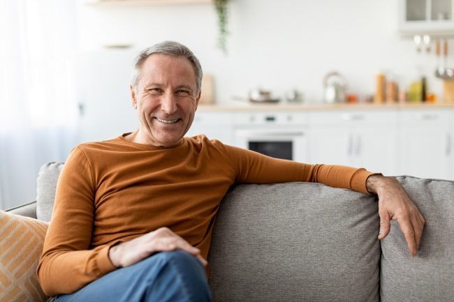 Mature man sitting on couch illustrates blog "Is Medicare Advantage Private Insurance?"